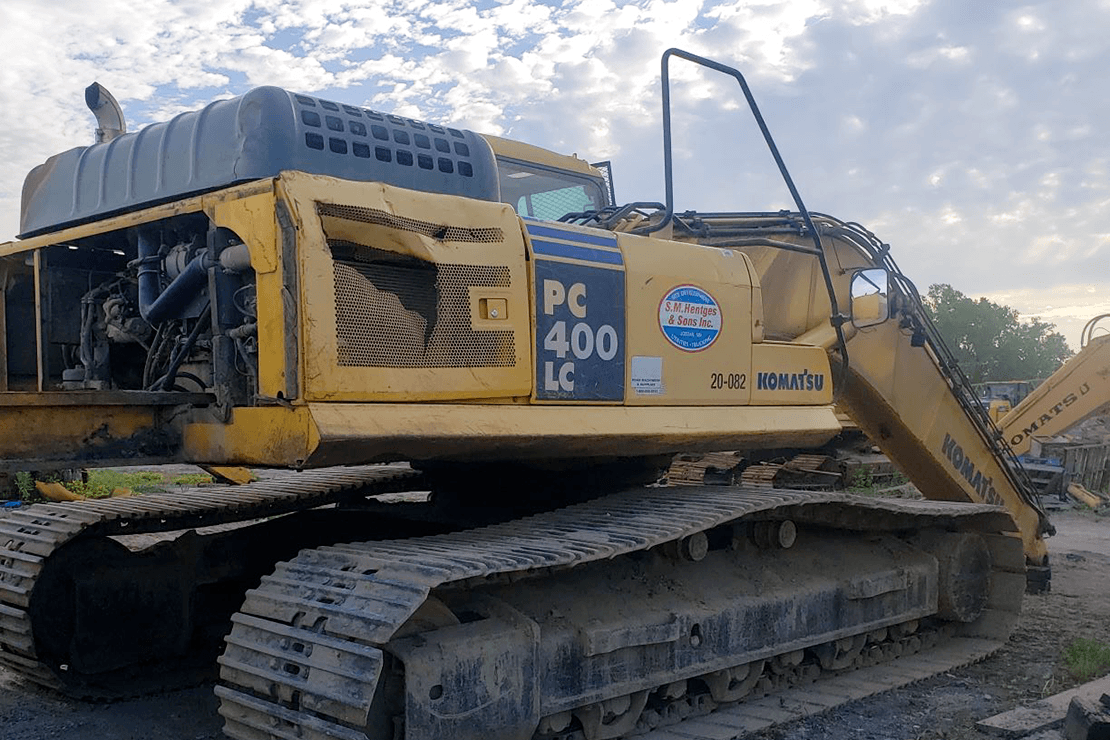 Excavator parked in foreground with blue sky and green trees in the background