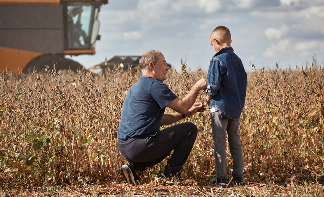 A farmer kneels happily beside his son in the middle of a field.