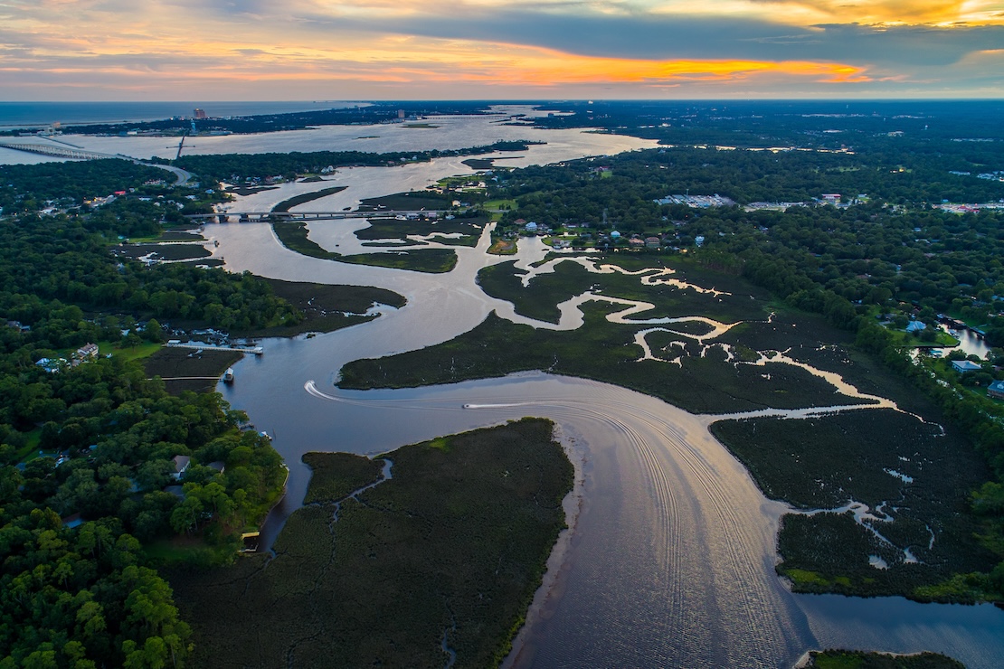 Aerial view of the Mississippi River Basin with boats on the river, trees along the banks, tributaries flowing into the river, and a sunset.